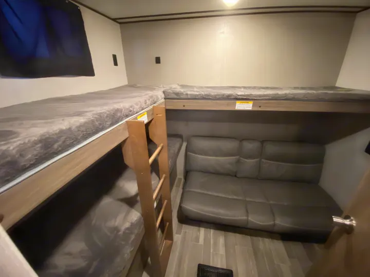 RV rental interior featuring practical bunk beds, a comfortable sofa, and wood-look flooring for a versatile space.. Keystone Crossroads Zinger 2021