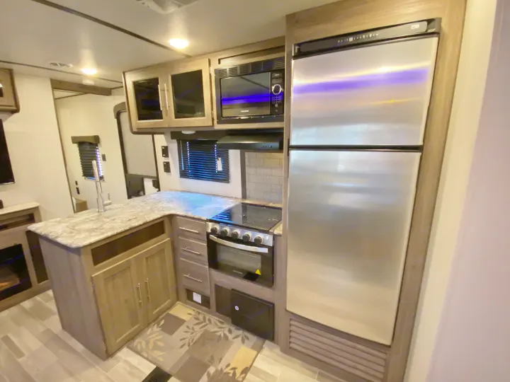 Modern RV rental kitchen featuring stainless steel appliances, L-shaped counter, and sleek cabinetry for travel.. Keystone Crossroads Zinger 2021