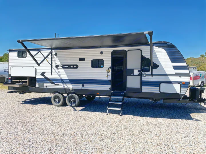 A Zinger travel trailer RV rental, complete with a deployed awning, open door, and exterior kitchen.. Keystone Crossroads Zinger 2021