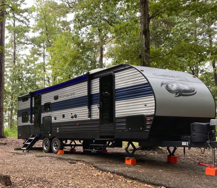 Modern gray and blue Cherokee travel trailer set up in a wooded campsite, ideal for your next rv rental getaway.. Forest River Cherokee 2021
