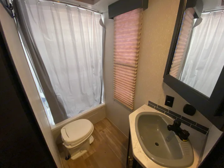 Explore this compact RV rental bathroom, equipped with a toilet, shower curtain, sink, and blinds. Functional space for your journey.. Forest River Cherokee 2021