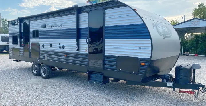 This image features a gray and black Cherokee Limited travel trailer RV rental with a blue stripe, on a gravel lot.. Forest River Cherokee 2021