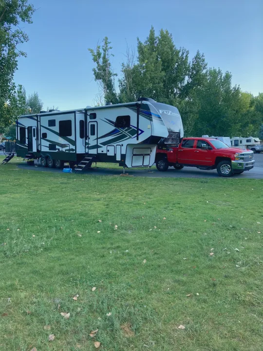 Red truck and white fifth-wheel RV at a spacious campsite, perfect for your next rv rental adventure.. Keystone Fuzion 2021