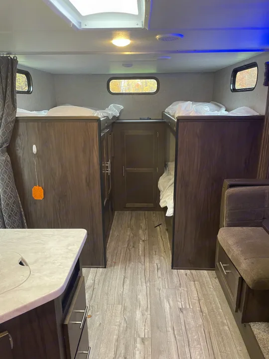 Inside an RV rental: four bunk beds, central aisle, kitchen counter, and sofa offer cozy camper living.. Forest River Cherokee Grey Wolf 2019