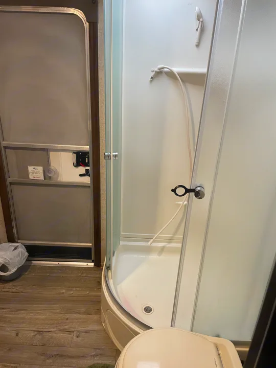 Compact RV rental bathroom with a curved glass shower, white toilet, and interior screen door.. Forest River Cherokee Grey Wolf 2019