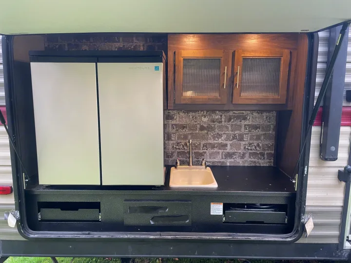Explore this RV rental's outdoor kitchen: a fridge, sink, countertop, and hidden stove for convenient camping and travel.. Forest River Cherokee Grey Wolf 2019
