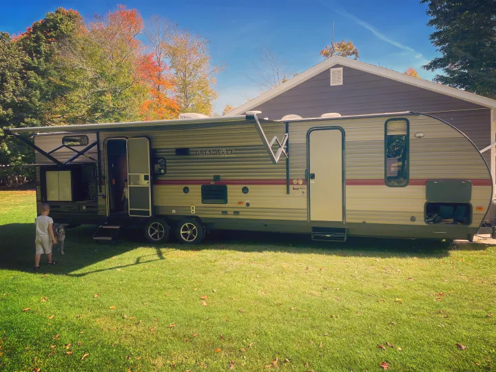 Family fun with an RV rental! This Grey Wolf travel trailer is set up on a grassy lawn with a child & dog. Autumn scene.. Forest River Cherokee Grey Wolf 2019