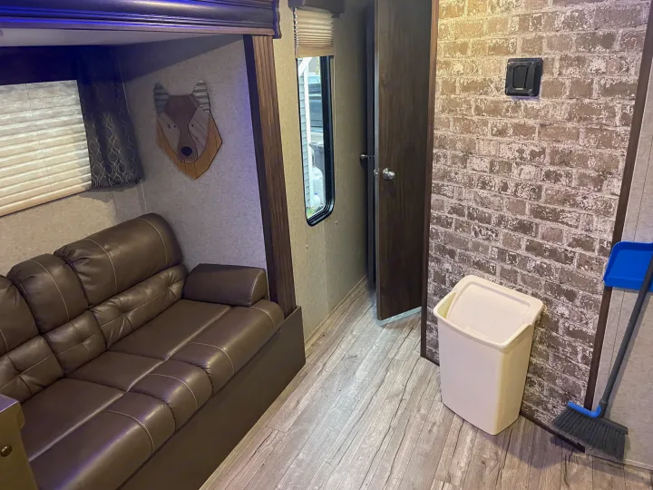 RV rental interior featuring a comfy brown leather sofa, bunk bed, window with blinds, and unique wolf wall art on patterned wall.. Forest River Cherokee Grey Wolf 2019