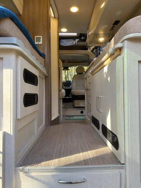 Spacious RV rental interior featuring light wood cabinetry, a sleeping area, and a clear view to the driver's cabin and outdoors.. Thor Motor Coach Rize 2022