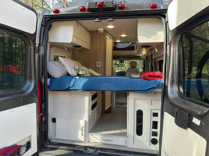 Spacious RV rental interior featuring a cozy bed, cabinetry, and controls, viewed from the open rear doors. Ideal for adventures.. Thor Motor Coach Rize 2022