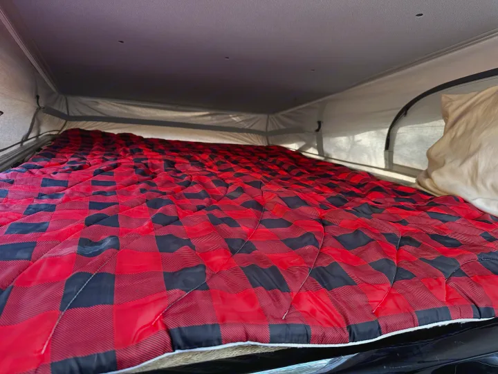 Cozy RV rental sleeping area with a vibrant red and black buffalo plaid comforter, ideal for comfortable camping trips.. Thor Motor Coach Rize 2022