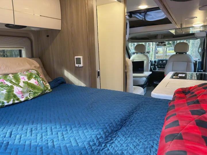Inside a spacious RV rental: a plush bed with a flamingo pillow, functional kitchen, and front cockpit. Ready for travel!. Thor Motor Coach Rize 2022