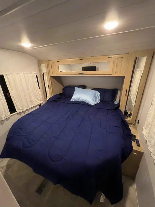 Cozy RV rental bedroom interior with a navy bed, pillows, and overhead storage. Ready for a comfortable night's sleep.. Forest River 31KQBTS 2024