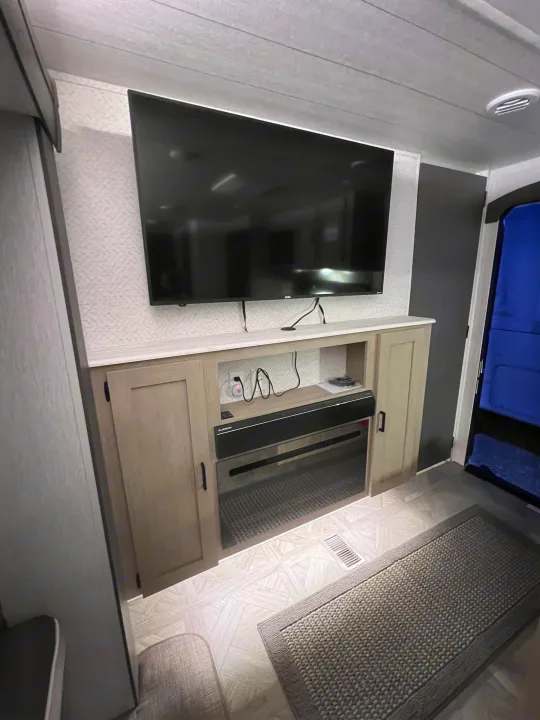 Modern RV rental entertainment center with TV, electric fireplace, and soundbar. Features clean decor and cozy amenities.. Forest River 31KQBTS 2024