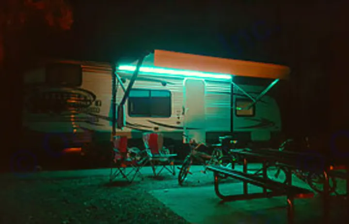 Night camping with an RV rental. A well-lit RV awning illuminates chairs, a picnic table, and a bike at the campsite.. Forest River Cruise Lite 2017