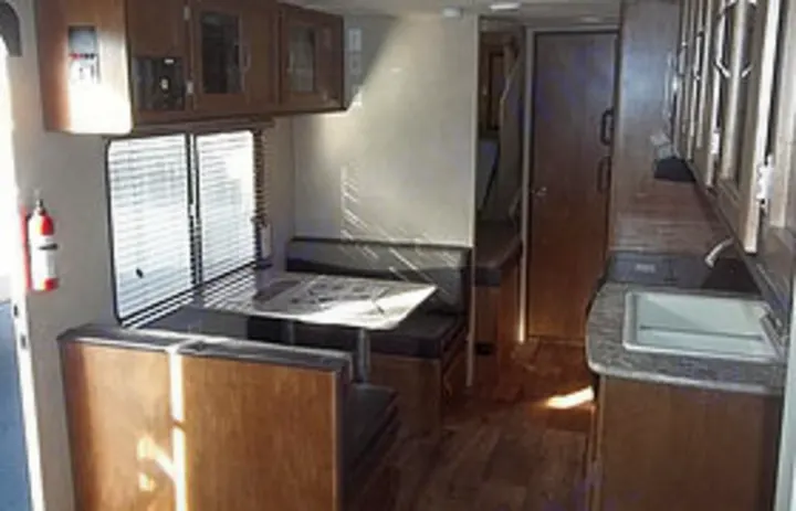 Bright RV rental interior showing a dinette with windows on the left and a kitchen sink on the right. Ideal for travel.. Forest River Cruise Lite 2017