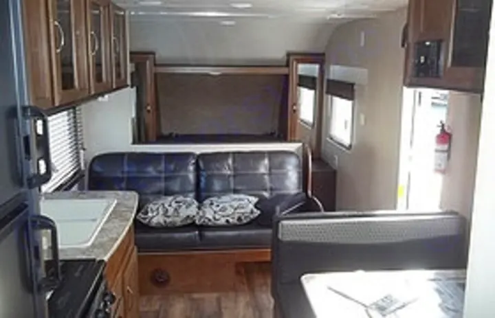 Inside this cozy RV rental: a camper's living area with a kitchen, black sofa, fold-up bed, and dinette.. Forest River Cruise Lite 2017