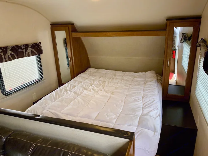 RV rental interior: A comfortable bedroom with a large bed, white comforter, wooden cabinets, and a window.. Forest River Cruise Lite 2017