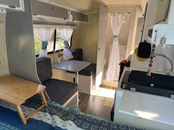 Cozy RV rental interior with a dinette, sunlit windows, a compact kitchen, bathroom with shower curtain, and sleeping area.. Casita Spirit 2023