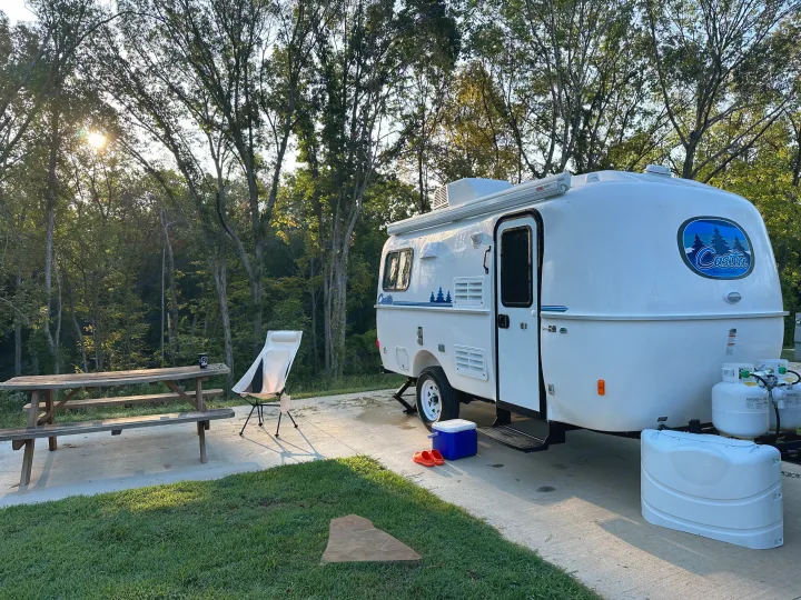 A white Casita travel trailer, an ideal RV rental, parked at a sunny campsite with a picnic table.. Casita Spirit 2023