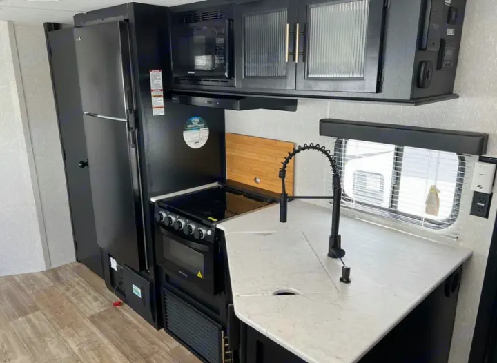 Inside an RV rental: a modern black and white kitchen with fridge, microwave, stove, and a spring-coil faucet.. Forest River Cherokee Grey Wolf 2021