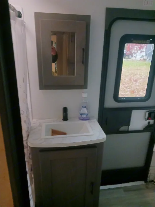 Inside an RV rental: compact bathroom vanity with sink, mirror, and an exterior door showing autumn foliage.. Embrace EL310 2021