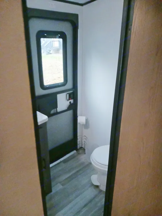 This RV rental interior features a compact bathroom with a toilet, a door leading outside, and modern wood-look flooring.. Embrace EL310 2021