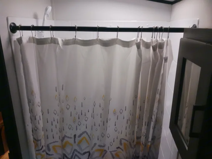 A white shower curtain with gray and yellow geometric patterns, hung on a black rod with silver hooks in an RV rental.. Embrace EL310 2021