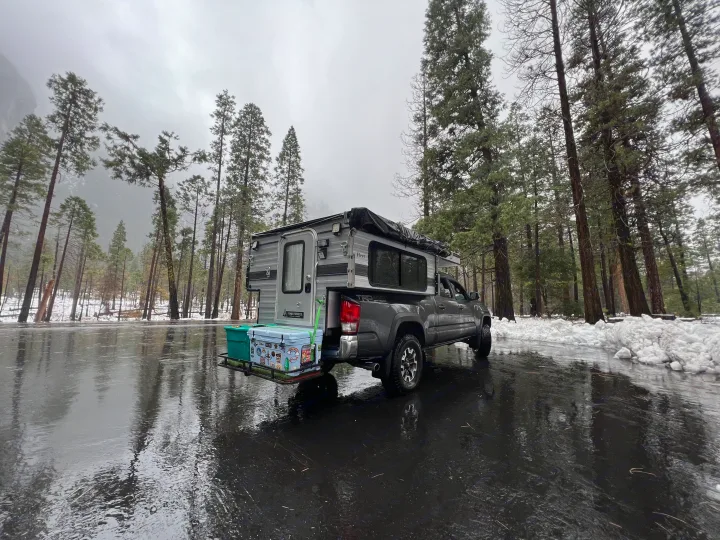 This RV rental truck camper is perfectly set for a snowy outdoor adventure, reflecting the forest in the wet road.. Four Wheel Campers Fleet 2021