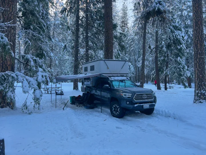 A truck with rooftop tent, an RV rental alternative, parked in a snowy forest campsite for winter camping.. Four Wheel Campers Fleet 2021
