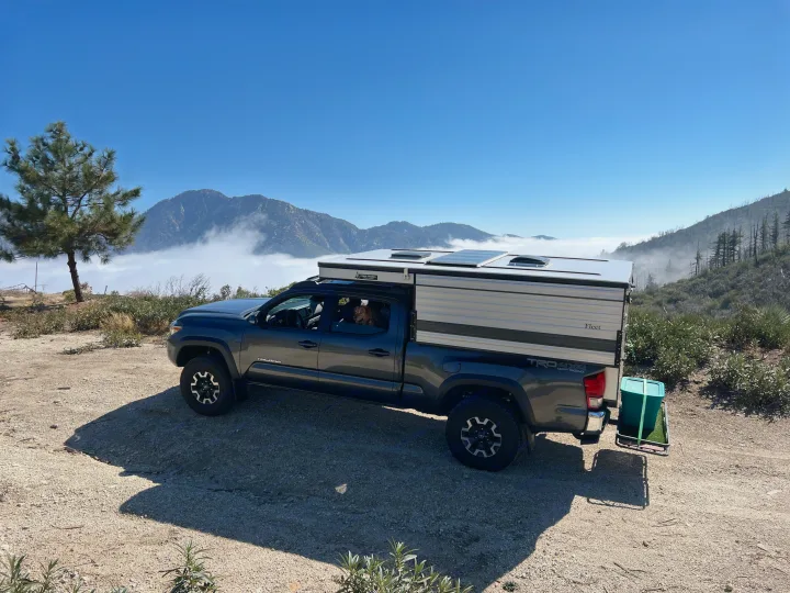 An RV rental-style Four Wheel truck camper on a Tacoma pickup, parked above the clouds in the mountains with a dog inside.. Four Wheel Campers Fleet 2021
