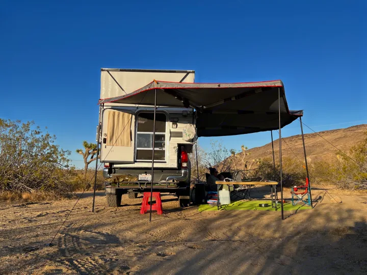 RV rental in a desert camp. A pop-up truck camper with an awning provides shade for a relaxed outdoor setup.. Four Wheel Campers Fleet 2021