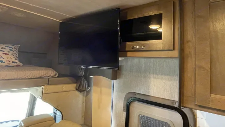 Cozy RV rental interior featuring an upper bunk bed with a pillow, a mounted TV, and built-in wooden cabinetry.. Nexus 35TSC 2020