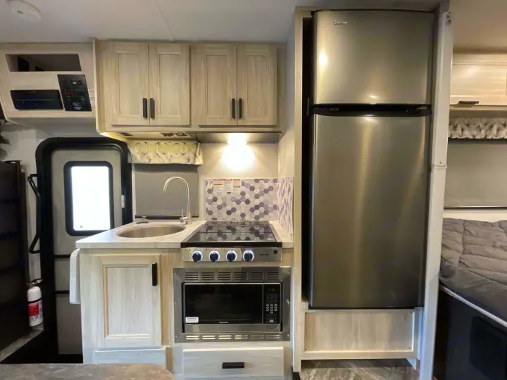 RV rental: The kitchen area features light-colored cabinets, a stainless steel fridge, microwave, cooktop, and sink, with a decorative backsplash.. Forest River Sunseeker 2022