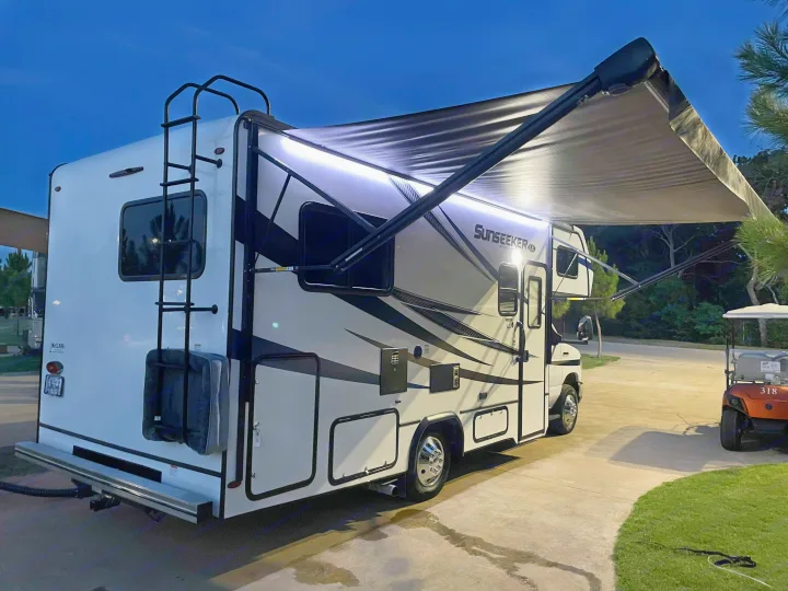 A white rv rental motorhome with its bright awning extended is parked at dusk, set for a comfortable night of camping.. Forest River Sunseeker 2022