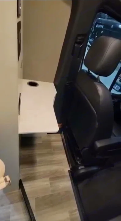 Inside an RV rental, a functional fold-down table with cup holder sits beside a black vehicle seat, showing a compact mobile workspace.. Cahaba Cahaba Class B 2022