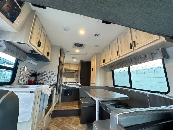 Modern rv rental interior with kitchen, dinette, and bedroom area, featuring light wood cabinets and gray upholstery.. Forest River Sunseeker 2022