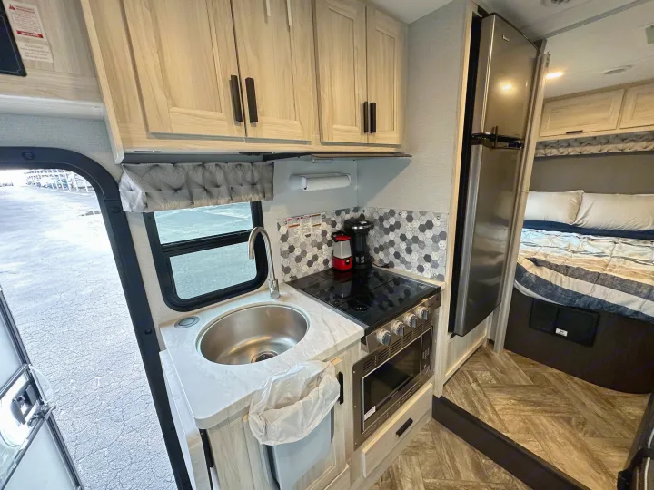 Bright, modern RV rental interior featuring a compact kitchen with full amenities, light wood cabinets, and a cozy bedroom.. Forest River Sunseeker 2022