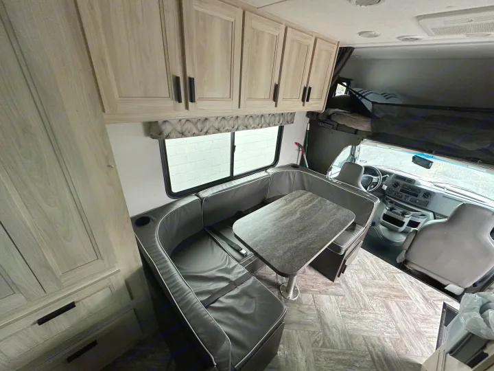 Inside a modern RV rental: light wood cabinets, gray U-shaped dinette with table, and front cockpit area visible.. Forest River Sunseeker 2022