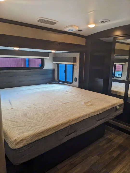 Comfortable RV rental bedroom showcasing a large mattress, dark wood headboard, and modern interior design.. Jayco North Point 2021