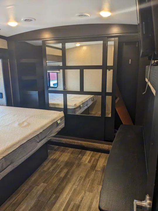 Inside a comfortable RV rental bedroom, showing a main bed, wood-look flooring, and a separate bunk area.. Jayco North Point 2021