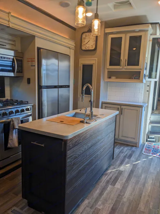 Spacious RV rental kitchen: island with sink, stainless steel fridge/oven, bright counters, wood-look floor, and white cabinets.. Jayco North Point 2021