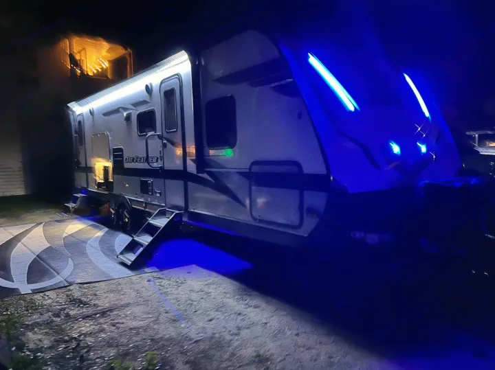 A Jay Feather RV rental brightly lit at night with blue and white lights, parked on a patterned mat.. Jayco Jay Feather 2022