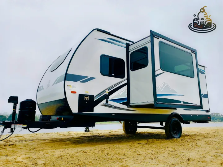 Experience beachside living with this sleek white and black RV rental, featuring a slide-out, parked on golden sand.. Forest River Surveyor Legend 2023