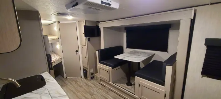 Inside a clean RV rental, showcasing bunk beds, a TV, dinette with table, and kitchen counter. Ready for travel!. Forest River inc Apex 208 BHS 2024