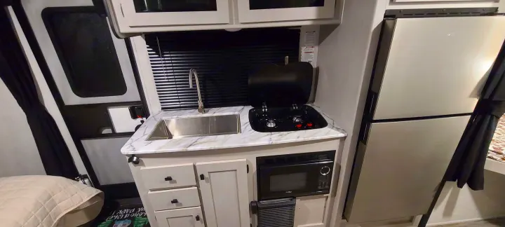 Compact RV rental kitchen features a sink, two-burner stove, microwave, and refrigerator for your travels.. Forest River inc Apex 208 BHS 2024