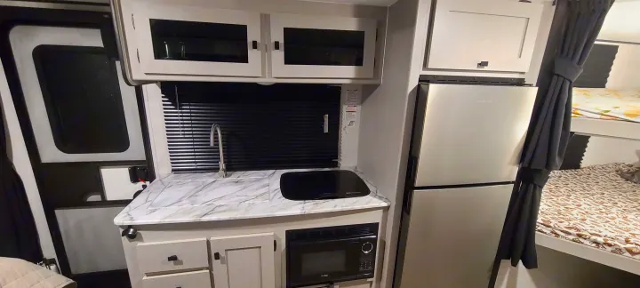 A compact kitchen area (left), a refrigerator (center right), and bunk beds (far right) are visible in this RV rental interior.. Forest River inc Apex 208 BHS 2024