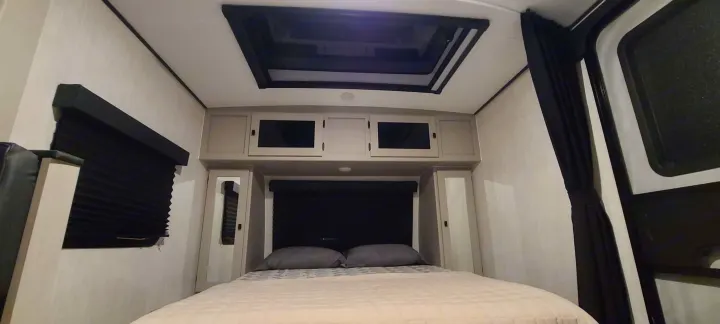 RV rental bedroom: bed, overhead cabinets, skylight, and dark pleated window blinds.. Forest River inc Apex 208 BHS 2024