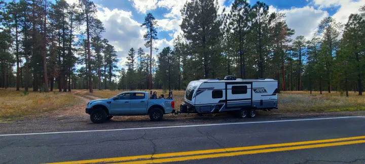 Family road trip: Light blue pickup towing an Apex RV rental, parked on a forest roadside.. Forest River inc Apex 208 BHS 2024