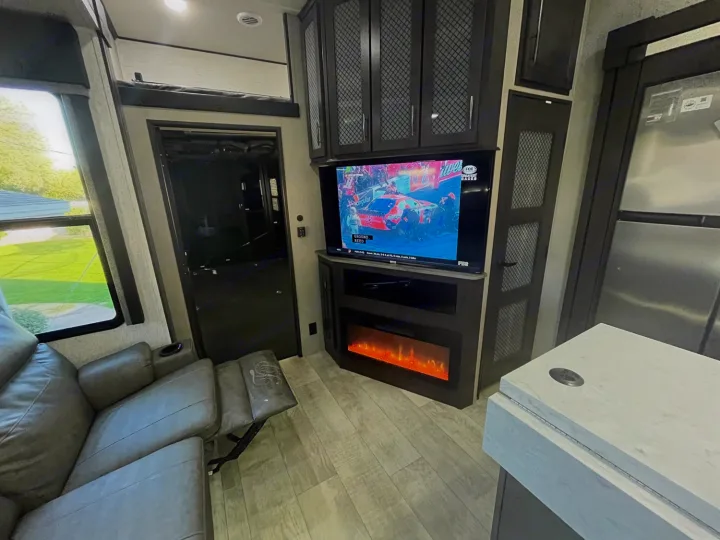 Cozy RV rental living space with TV, electric fireplace, and recliner. Enjoy comfort and entertainment on your travels.. Grand Design Momentum M-Class Toy Hauler 2022
